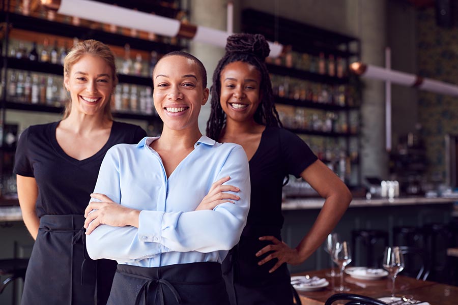 Business Insurance - Three Women, an Owner and Two Waitresses, Standing in a Restaurant With Tables Set Behind Them